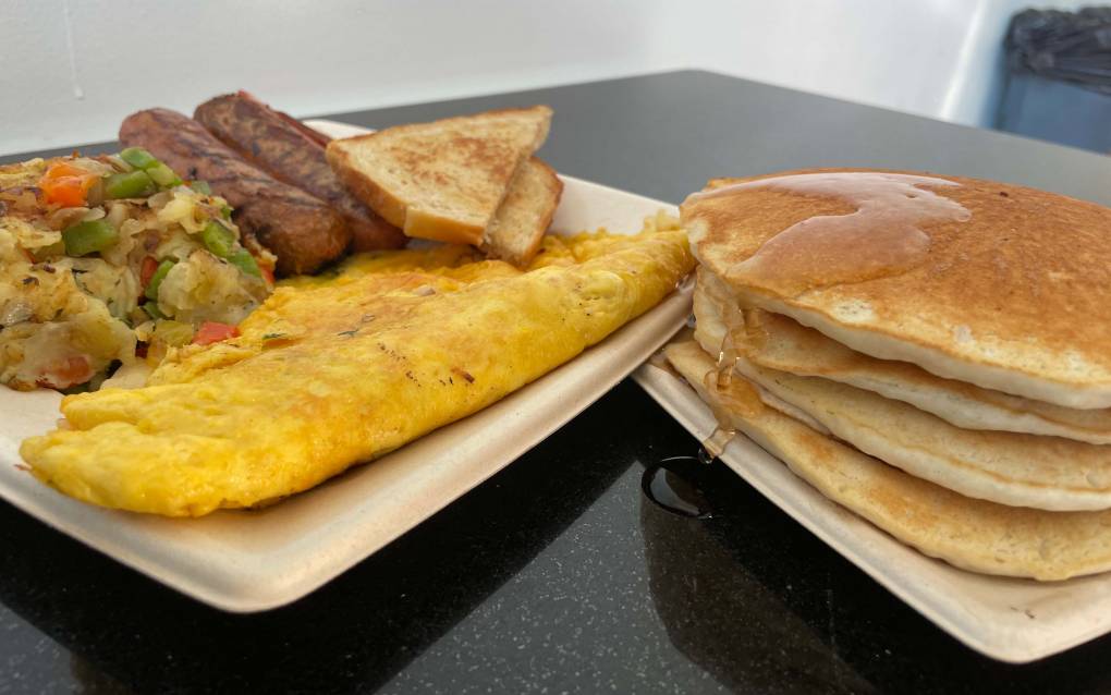 Sausage, omelette and breakfast potatoes on a plate next to a stack of pancakes.