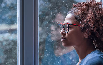 A woman staring out the window while it’s snowing.