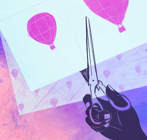 A hand holding scissors and cutting out paper for a scrapbook