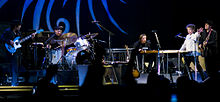 Dylan together with five members of his band onstage. Dylan, dressed in a white shirt and black pants, is second from right.