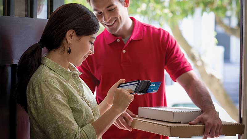 Man delivering pizza and a woman paying with her Visa card.