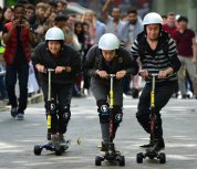 Three students racing on motorised scooters