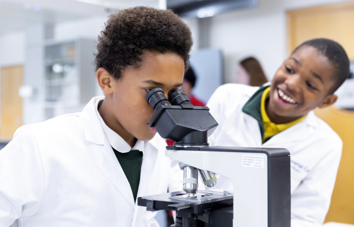 Two primary school age boys look down a microscope.