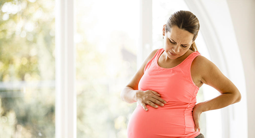 woman in early labour sitting on a birth ball and rubbing her back and belly