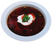 A bowl of dark-red borscht garnished with a dollop of sour cream and a parsley leaf