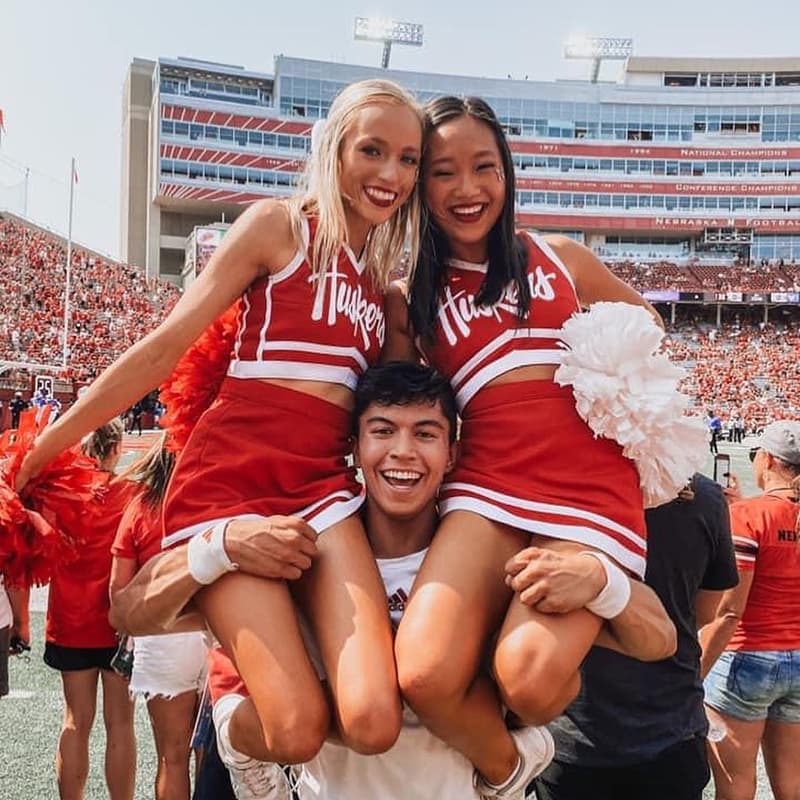 Two cheerleaders sit atop the shoulders of another cheerleader on the field at Memorial Stadium.