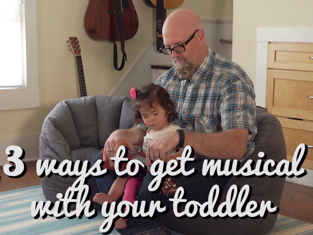 Toddler sat on dad's lap with small guitar