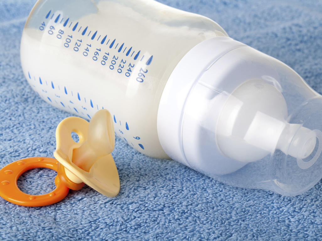 milk-filled baby bottle and orange dummy lying on blue towel