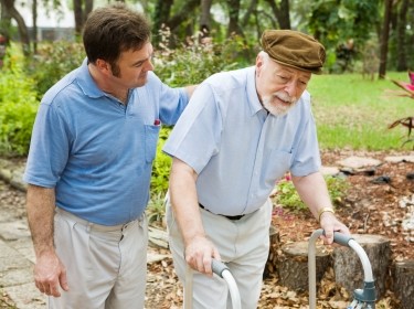 A younger man helping an elderly man who is using a walker