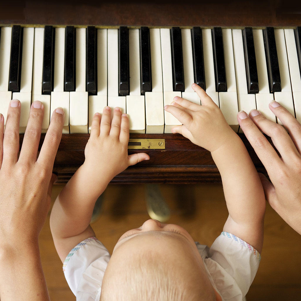 young child sitting with adult while they put their hands on piano keys