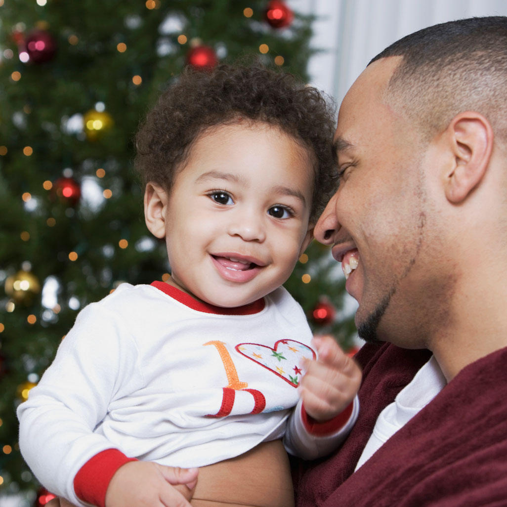 man holding young child with christmas tree behind them