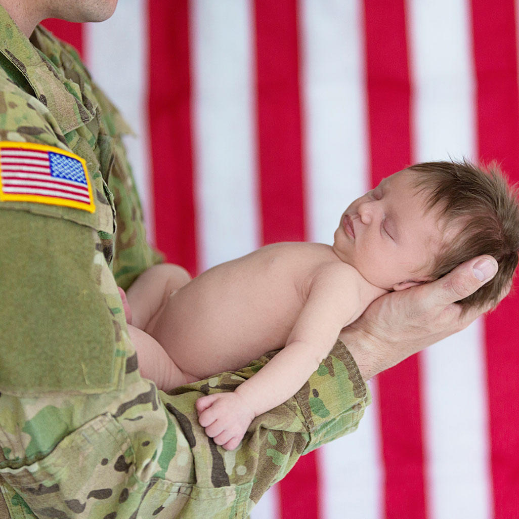 military service person holding a sleeping newborn baby on his forearm