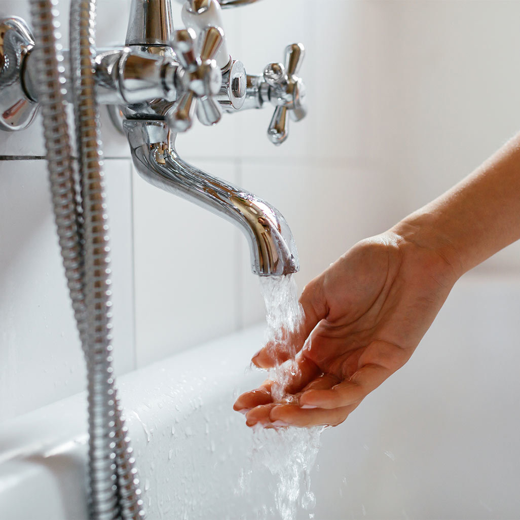 A woman's hand checking the water from a bathtub faucet.