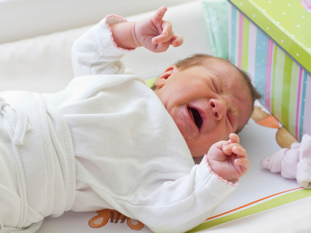 crying baby laying on its back in the crib