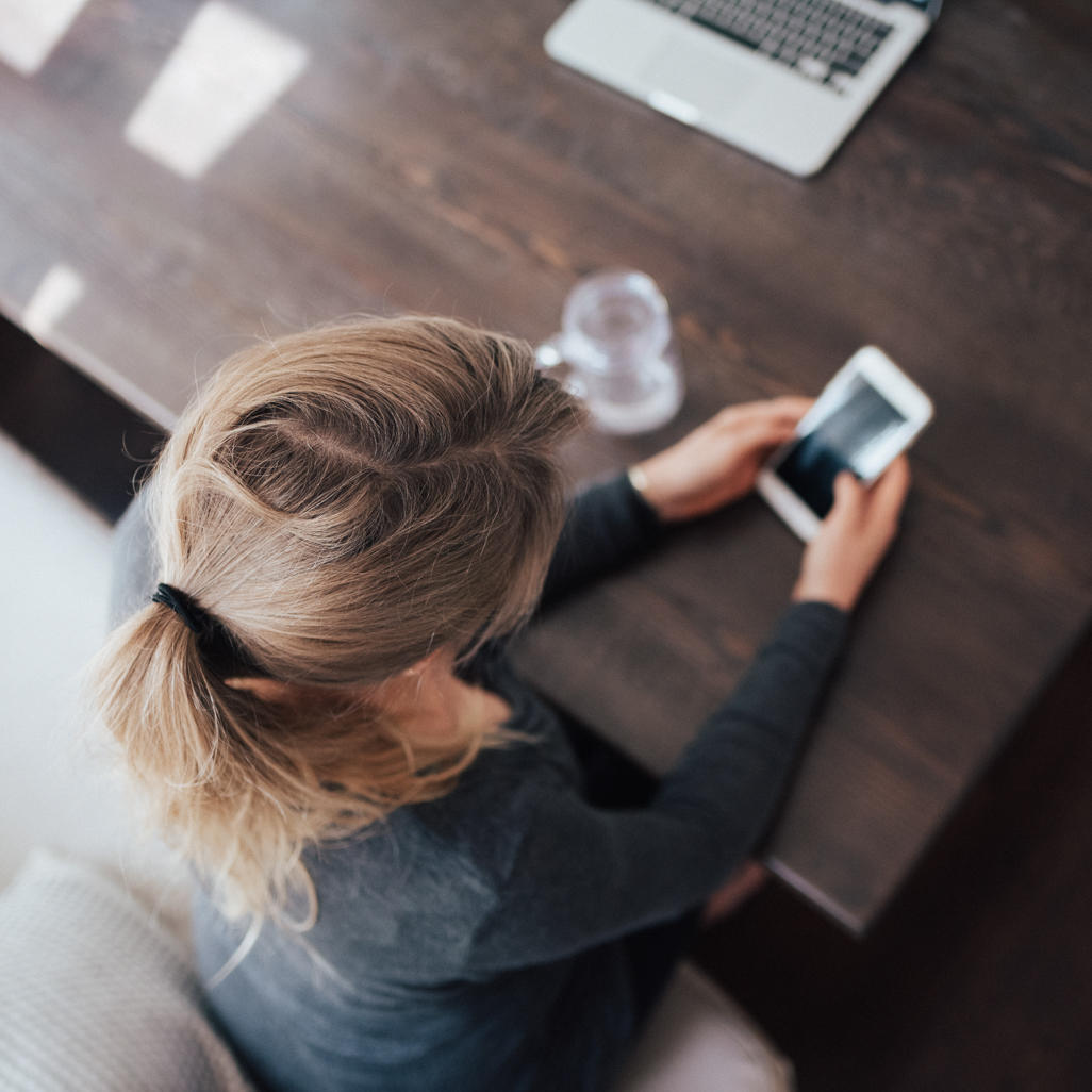 An aerial view of a woman sitting at a desk, looking at her phone.