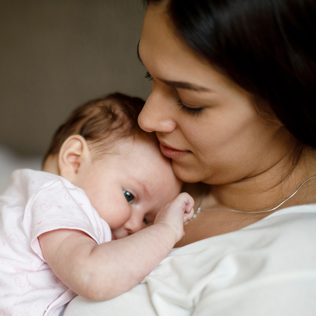 A postpartum mom cuddling her newborn baby.