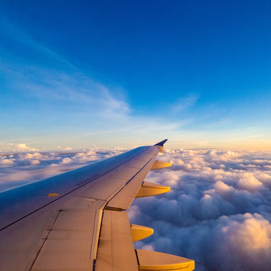 An airplane wing, with blue skies and clouds in the background.