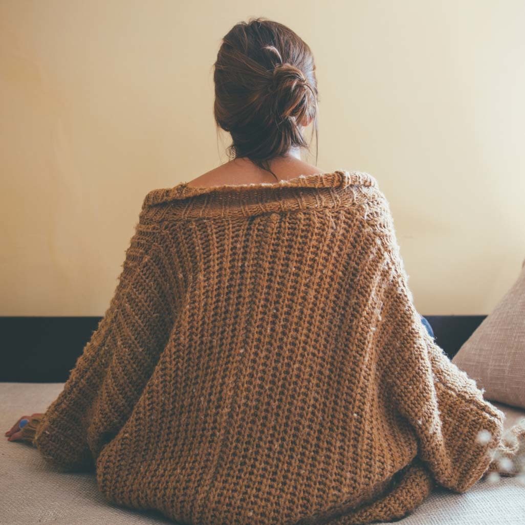 A woman sitting on the bed with a large sweater