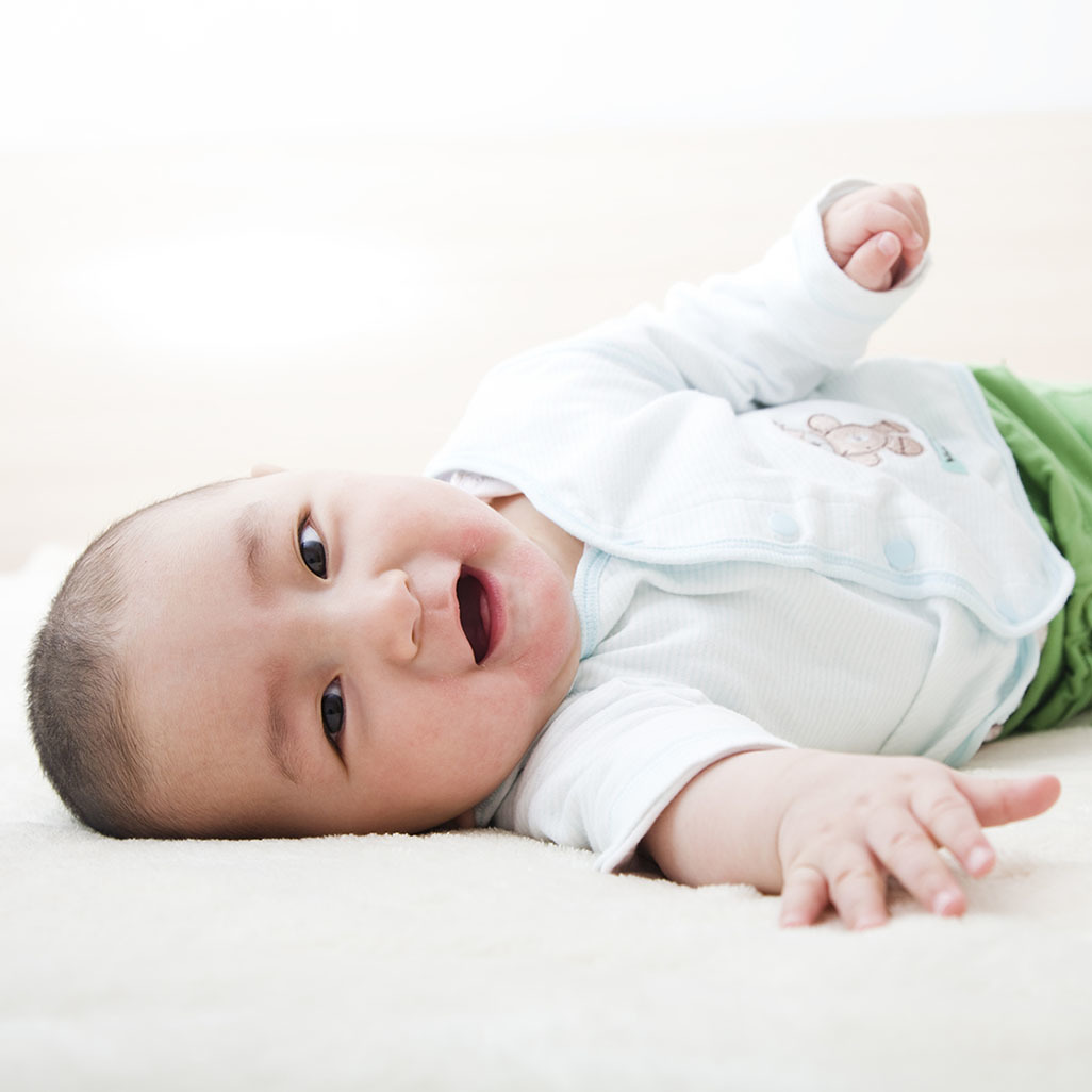 smiling baby on blanket trying to roll over