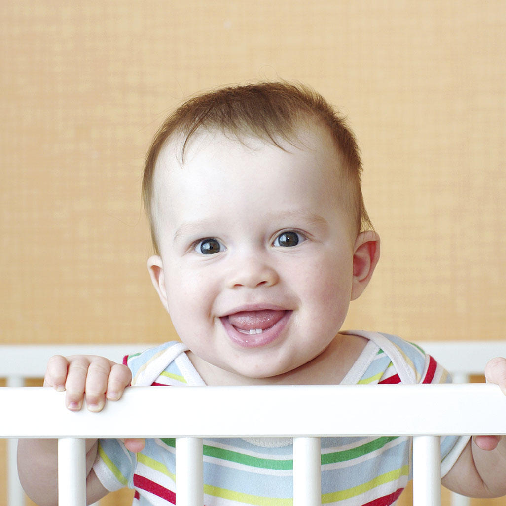 baby inside a crib holding on to the side and smiling