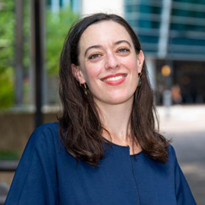 Hannah Bloch-Wehba - Assistant Professor of Law, Texas A&M. Wearing a dark blue shirt, with green trees over their shoulder.