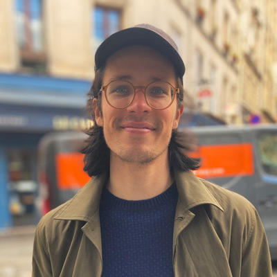 Robert Gorwa. Fellow, Centre for International Governance Innovation. Wearing a hat and light colored glasses, in a city center with a brown and orange truck in the near background.