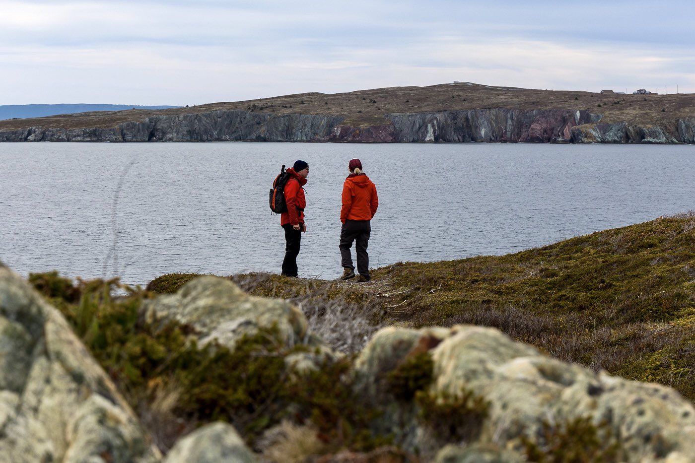 Two people dressed in red jackets discuss geology atop a cliff.