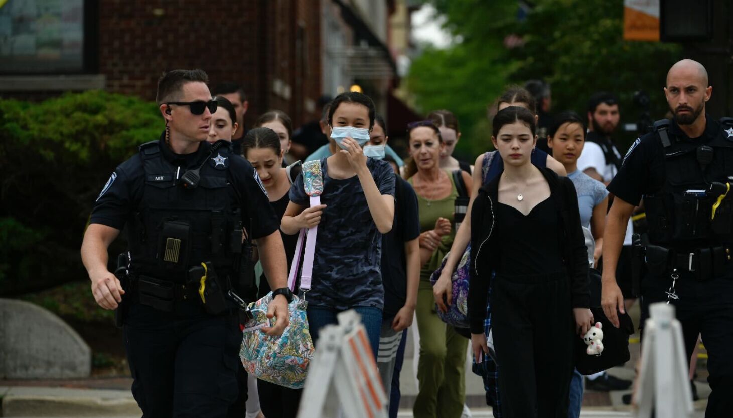 Police in Highland Park escort people Monday afternoon who had sought a safe place after a shooter with a high-powered rifle opened fire hours earlier at Highland Park’s Fourth of July parade.