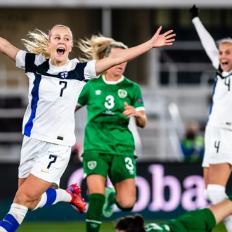 Two Finnish soccer players raise their hands in the air in triumph.