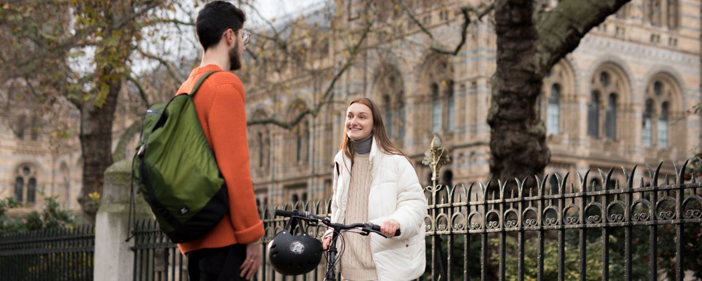 A young man and woman chat and smile. The young woman holds a bike.