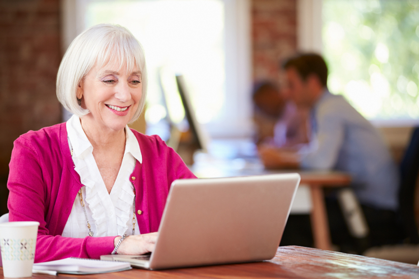 Happy Smiling Senior Woman Working At Laptop In Contemporary Office