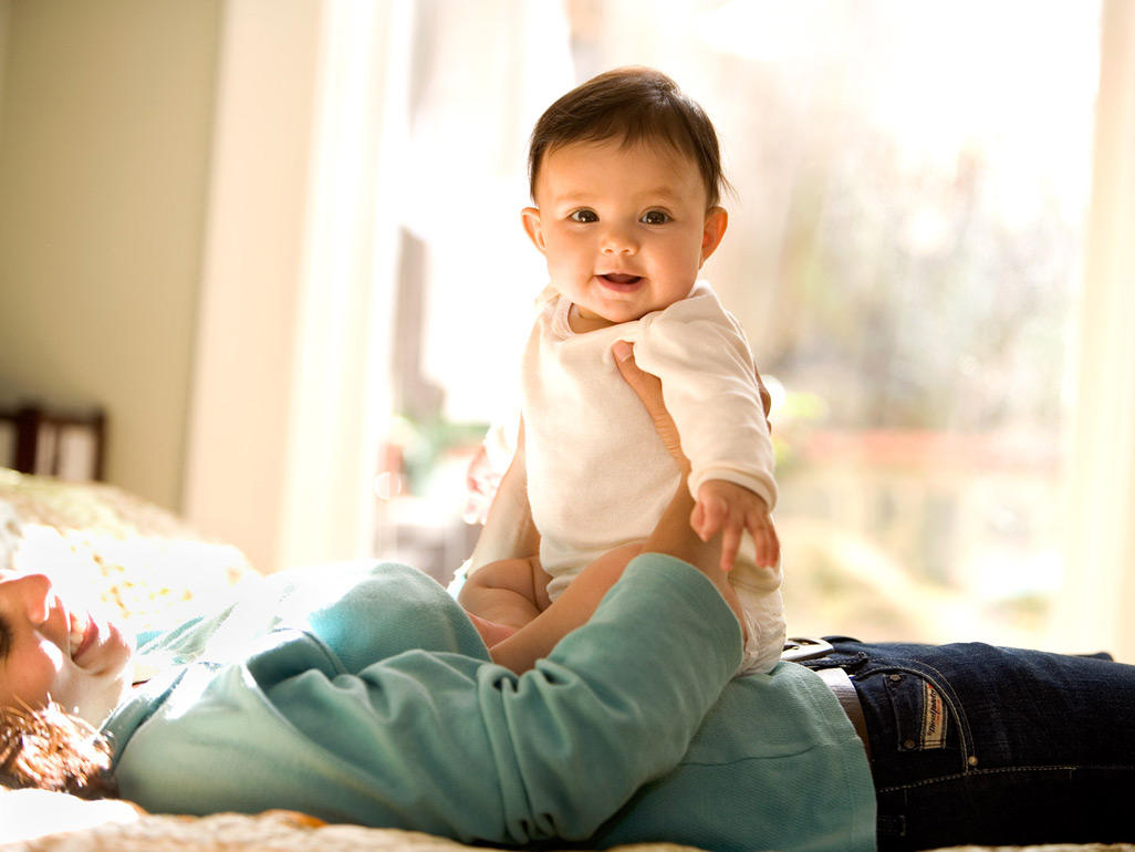 Mutter liegt auf dem Bett und hat Ihr Baby auf dem Bauch sitzen