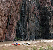 View of two small boats in a river, with high cliffs rising immediately behind them