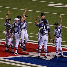 Seven officials are pictured meeting at the infield. Officials meeting at midfield