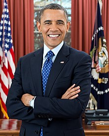 Obama standing with his arms folded and smiling.