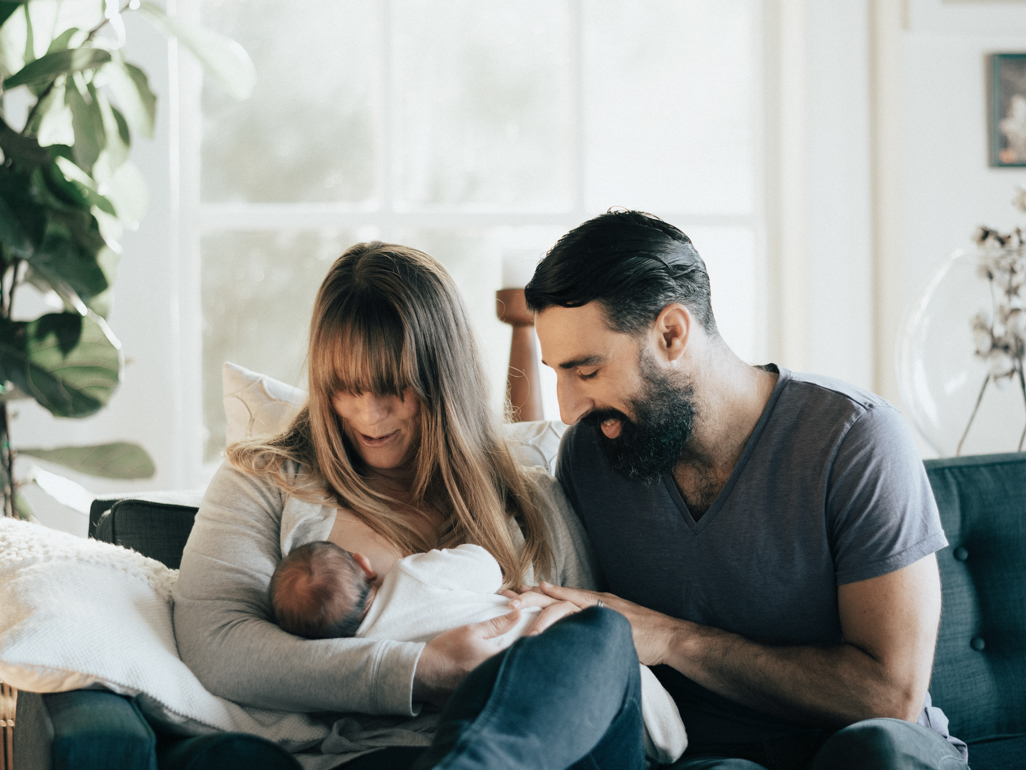 New mom and dad holding an infant while sitting down on a couch