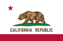 The flag shows a red stripe on the bottom in a white field, with a red star on the top left in the canton. In the center, a grizzly bear is on top of a mound of green grass on over the white field. Below it, text reads "CALIFORNIA REPUBLIC" in a Seal color.