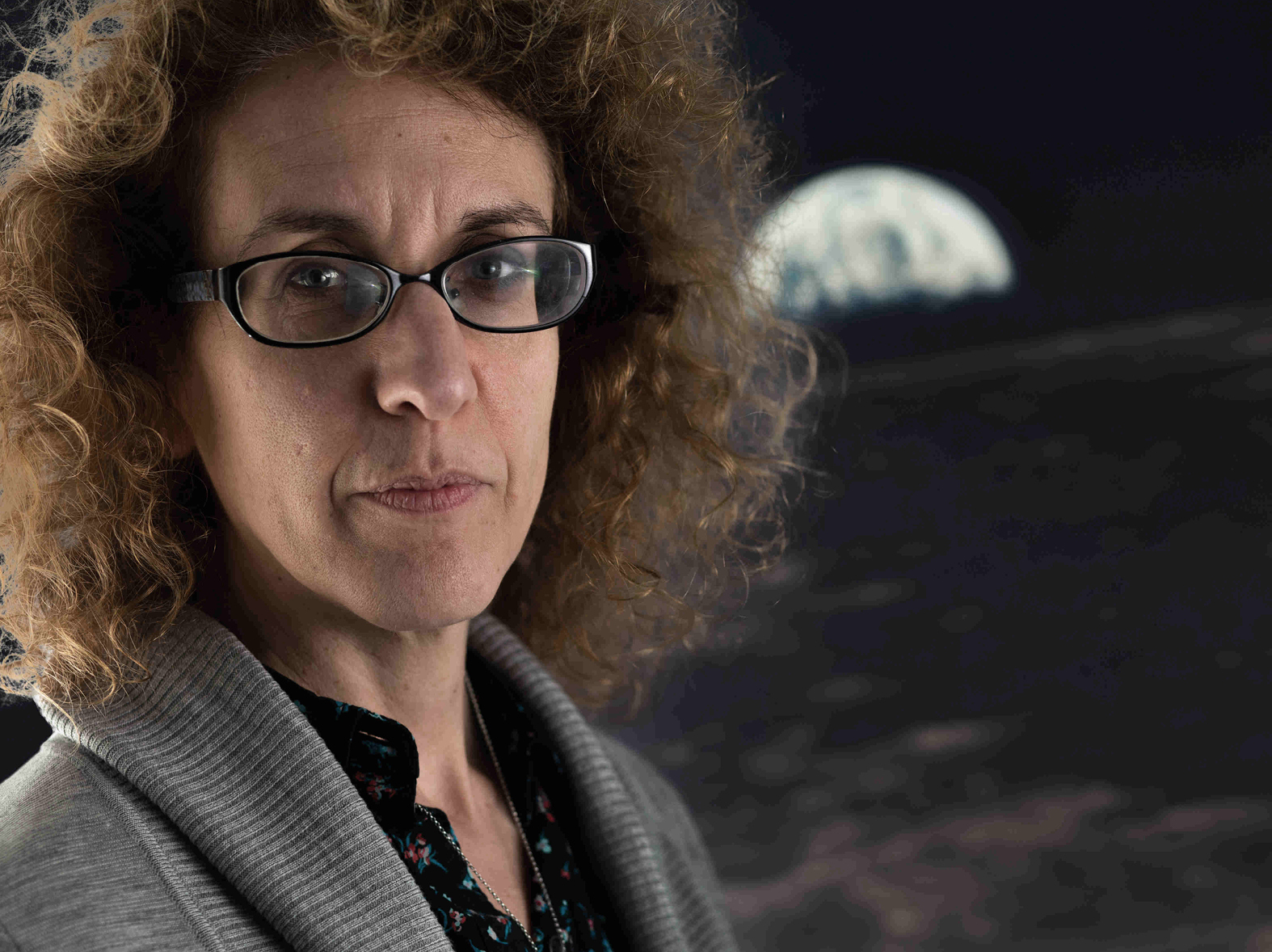 Professor Vicky Kaspi looking into the camera standing in front of a poster of the moon