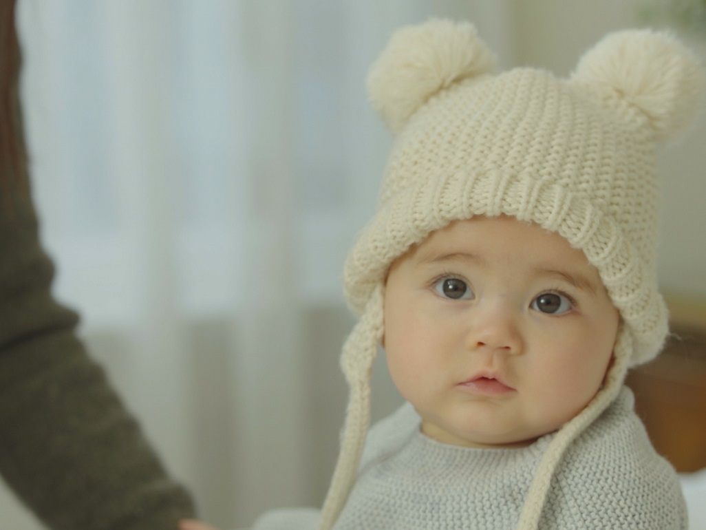 baby wearing a knit sweater and a knit hat with pom poms