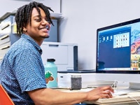 Young man in front of a laptop wearing a blue shirt and smiling