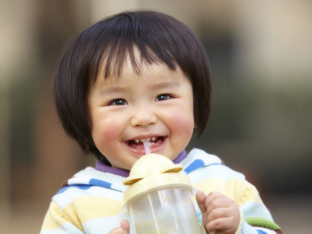 child smiling and drinking from a bottle using the straw