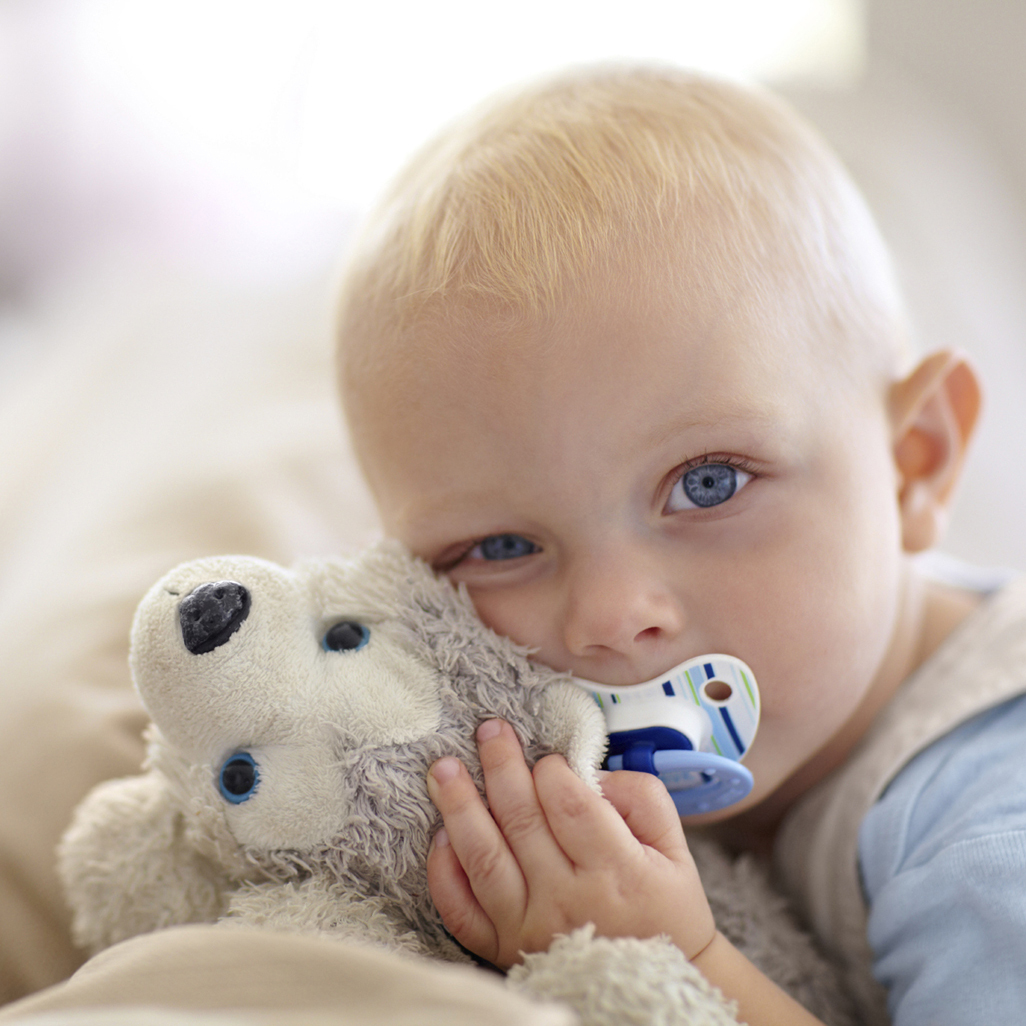 little boy with pacifier hugging his stuffed toy