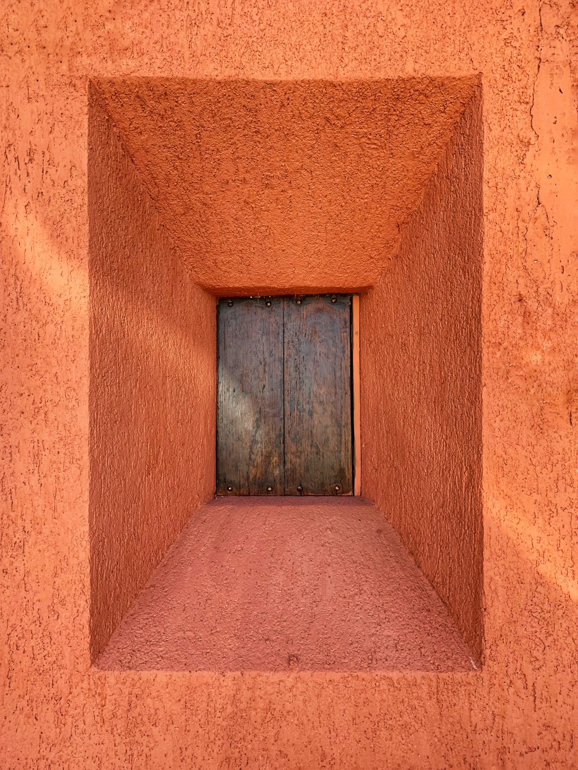 Small window covered in wood in the center of an orange wall.