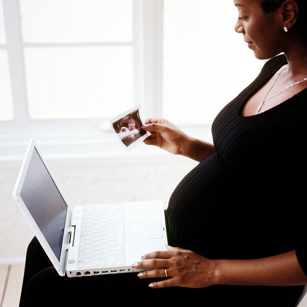 pregnant woman with a laptop looking at a ultrasound photo