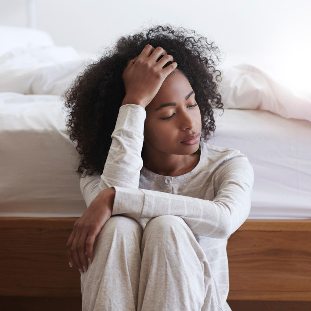 woman sitting on the floor next to her bed with feeling ill