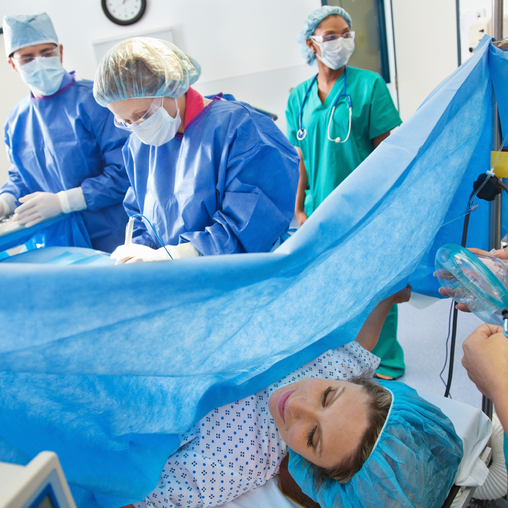 A surgeon and a nurse performing a c-section on a woman in an operating room