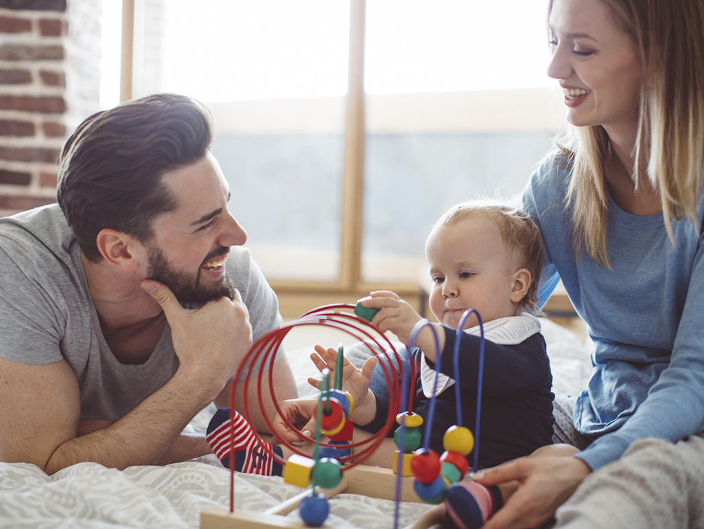 mother and father playing with their baby on a bed