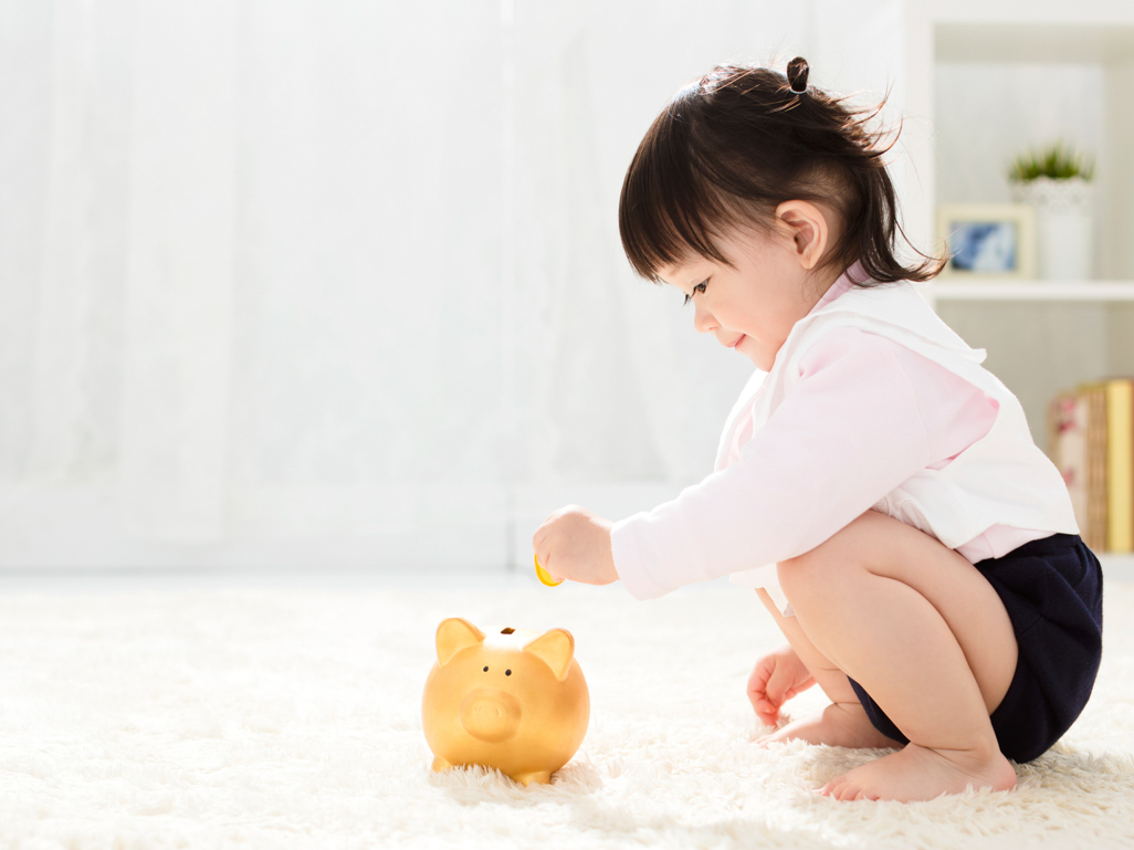 baby putting coins in piggy bank