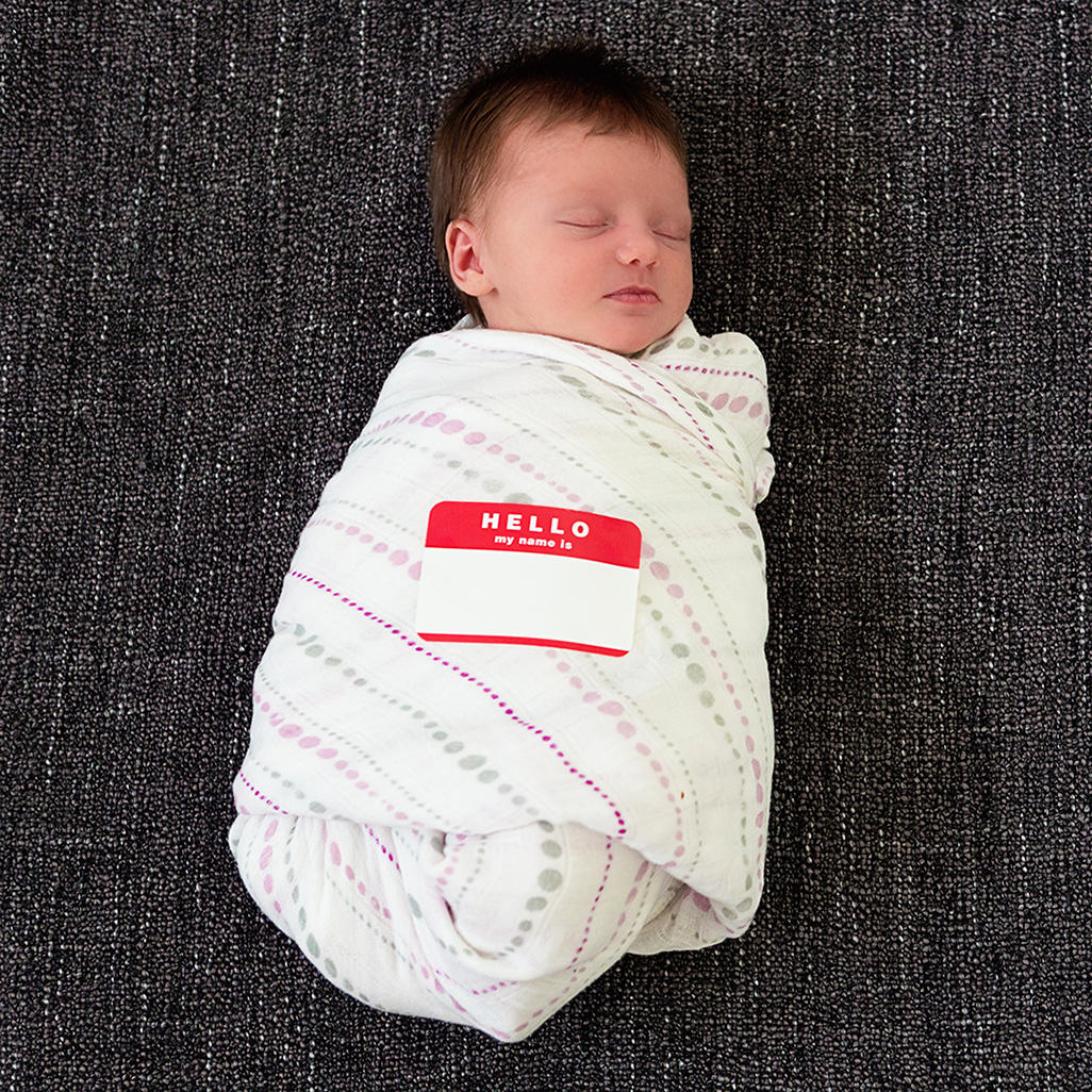 newborn baby in swaddle with sticker 'Hello my name is (blank)'