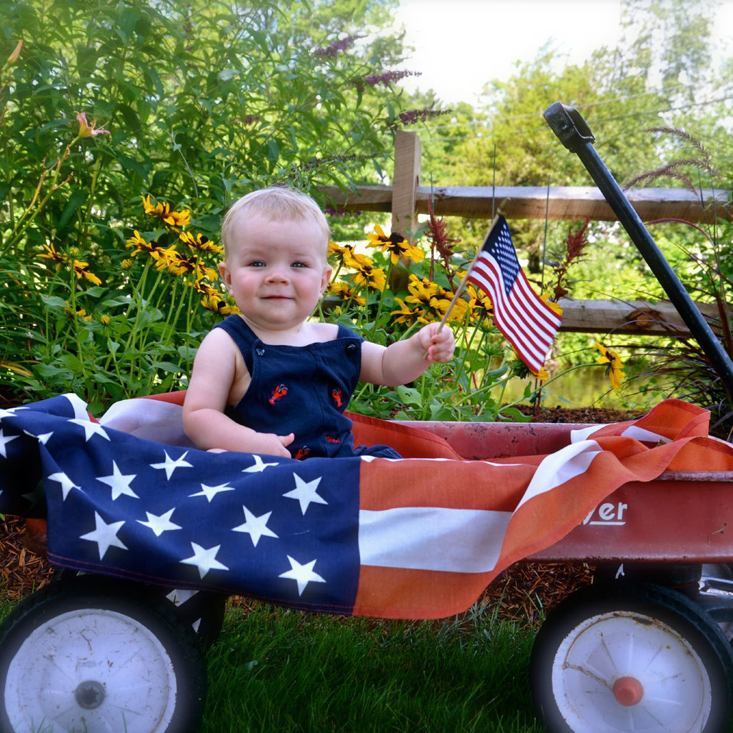 baby holding a small american flag sitting up in a wagon